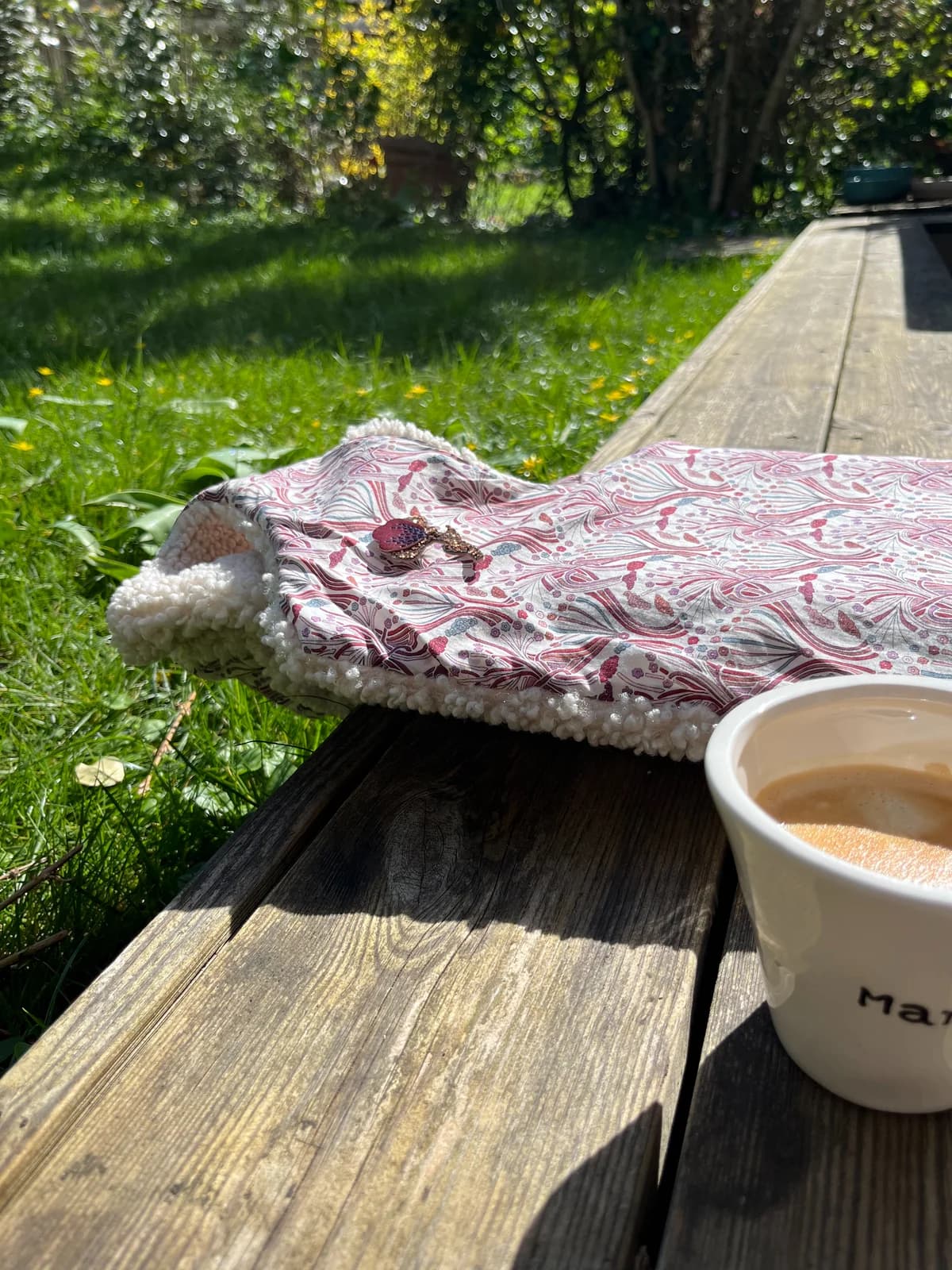 Col en tissu liberty rose à pompons posé sur une table de jardin avec café — By Mésange