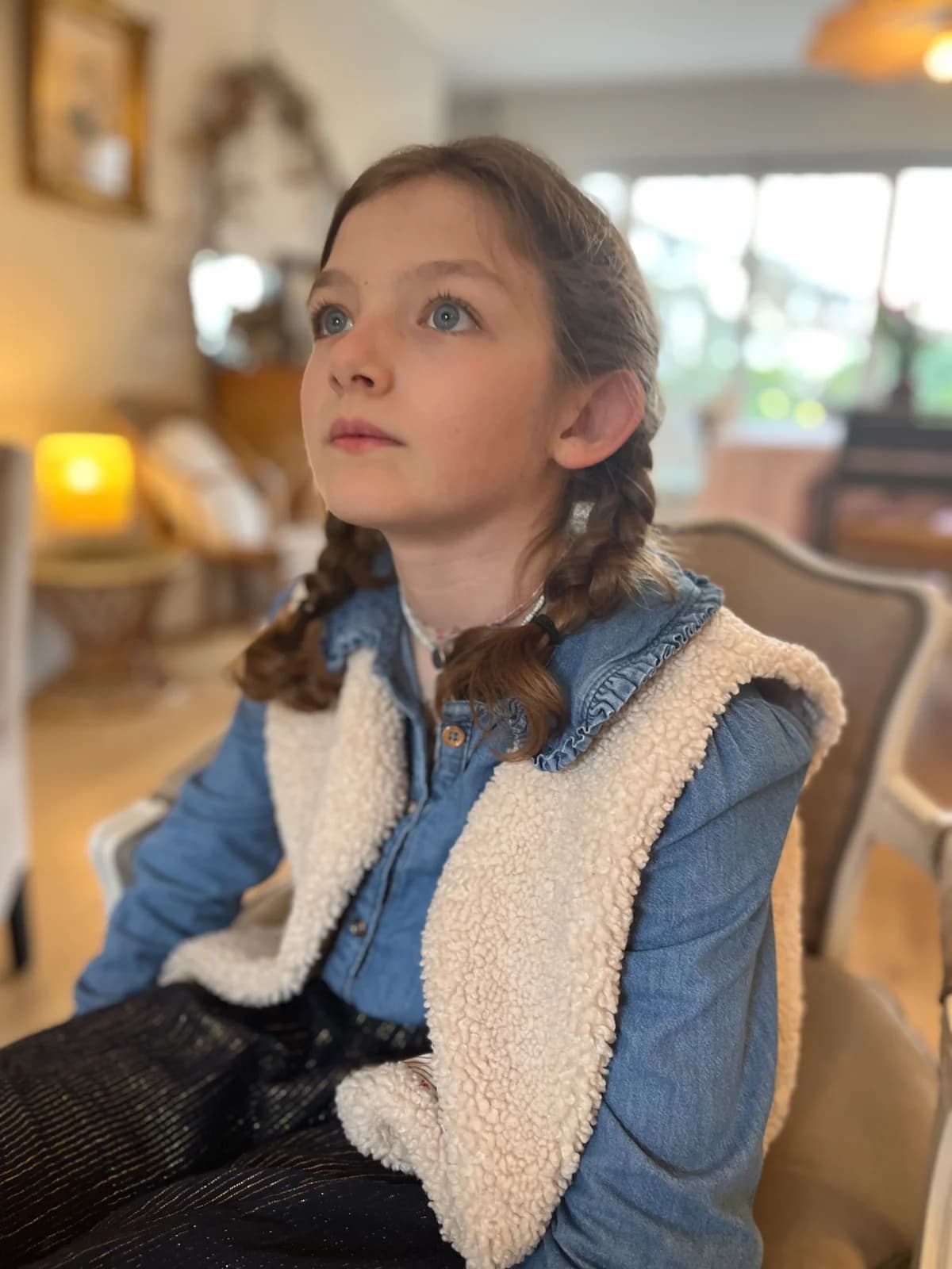 Fillette assise dans un fauteuil, blouse en jean et gilet berger, tresses — By Mésange