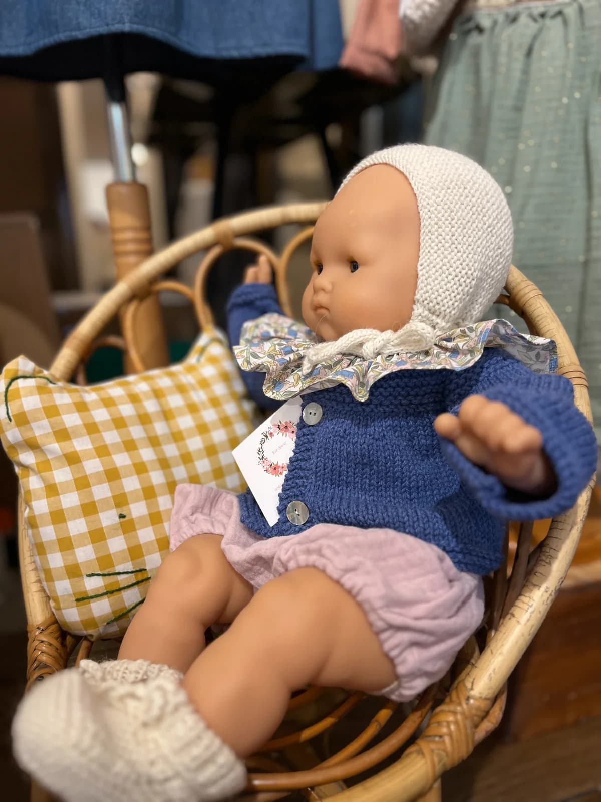 Poupée habillée By Mésange — cardigan bleu, col fleuri et bloomer rose dans un fauteuil en rotin