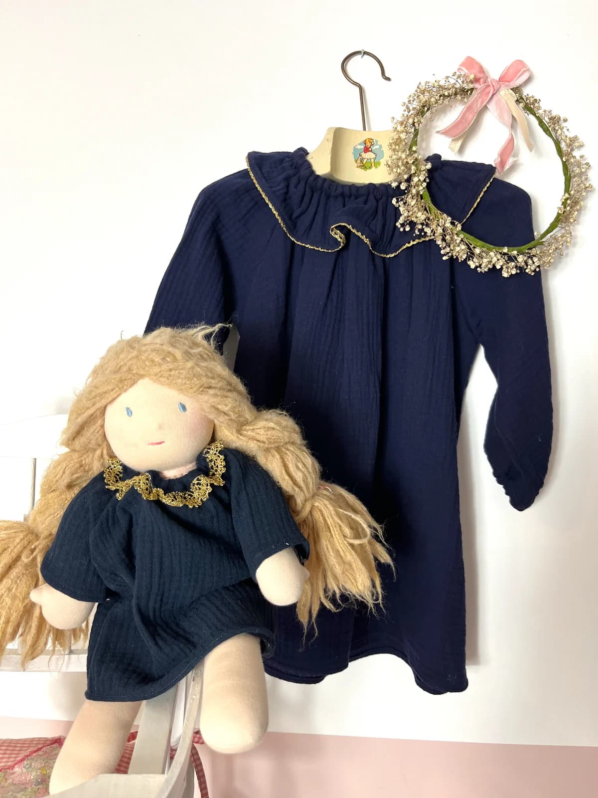 Robe enfant en gaze de coton bleu marine avec col doré, sur cintre avec couronne de fleurs séchées